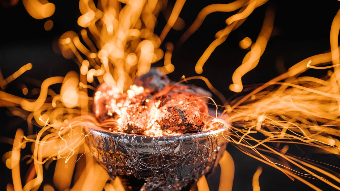 Carbuni aprinsi pe un creuzet acoperit cu folie de aluminiu, cu scantei portocalii in jur