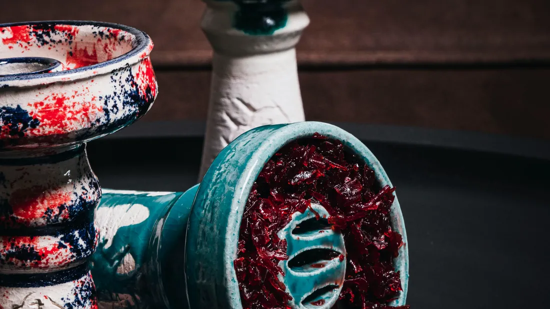 Creuzet de ceramica alb cu pete rosii si turcoaz, umplut cu tutun rosu inchis, pe o tava neagra